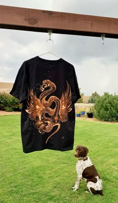 a dog sitting in the grass next to a t - shirt with a snake on it