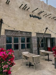 the outside of a restaurant with wooden tables and chairs in front of it, surrounded by pink flowers