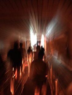 blurry photograph of people walking down a long hallway with lights on the walls and floor