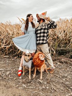 a man and woman standing next to each other in front of a cornfield with two dogs