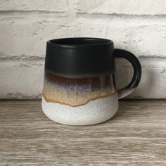 a black and white coffee mug sitting on top of a wooden table next to a brick wall