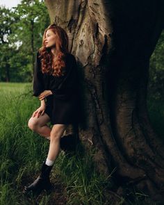 a woman sitting on the ground next to a tree with her legs crossed, looking up