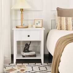 a white nightstand with a lamp on it next to a bed