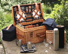 an open picnic basket sitting on top of a table next to wine glasses and other items