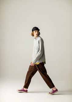 a young boy walking across a white floor wearing brown pants and a gray sweatshirt with yellow trim