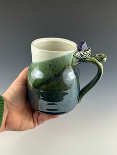 a hand holding a green and white coffee mug with a dragon handle on the inside