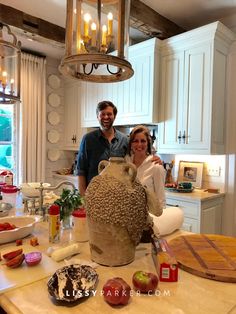 a man and woman standing next to a vase on a counter top in a kitchen