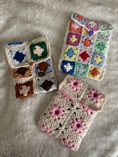 three crocheted items are laying on a white blanket, one has a flower and the other is a square