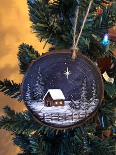 a christmas ornament hanging from a tree with a house in the snow on it