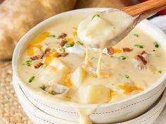 a spoon full of potato soup with cheese and bacon on top, in a white bowl