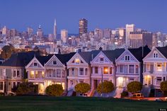 a row of painted victorian homes in san francisco, california with the city skyline in the background