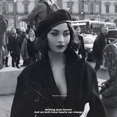 a black and white photo of a woman walking down the street with people in the background