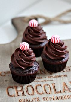 three cupcakes with chocolate frosting and candy canes sitting on top of a box