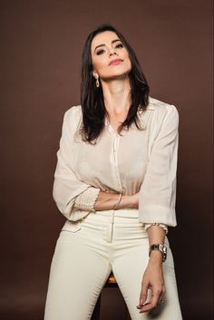 a woman posing for a photo with her arms crossed in front of her chest and wearing white pants