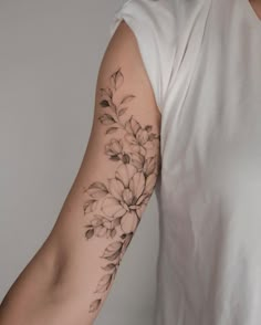 a woman's arm with flowers and leaves tattooed on the left side of her arm