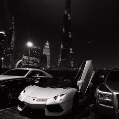 some very nice looking cars parked in front of a big city building at night time