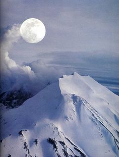 a full moon is seen above the snow covered mountain tops in this view from an airplane