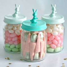 three jars filled with candy and marshmallows on top of a white table