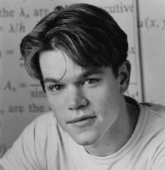 black and white photograph of a young man in front of a wall with writing on it