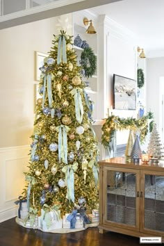 a decorated christmas tree with blue and gold ornaments in a living room area, surrounded by other holiday decorations