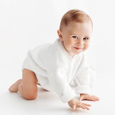 a baby is smiling while laying on the floor wearing a white sweater and leggings