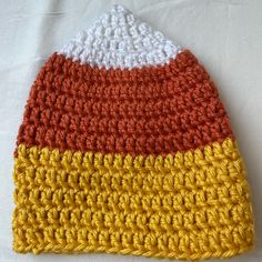 a crocheted hat is laying on a white tablecloth with orange, yellow and white stripes