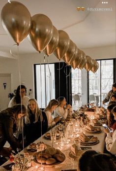 a group of people sitting around a long table with gold balloons hanging from the ceiling