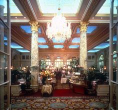 an ornate lobby with chandeliers and tables in the center is seen through open windows