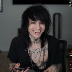 a man with black hair and tattoos on his chest smiling while holding a cell phone