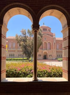 the view from inside an arched window at a building with flowers in front of it