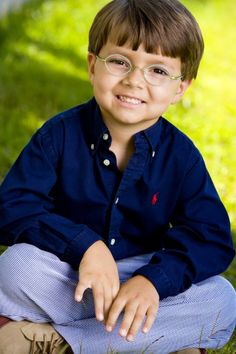 a young boy wearing glasses sitting in the grass