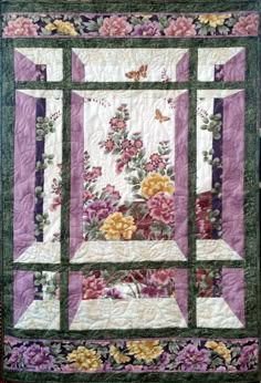 a quilted wall hanging with flowers and butterflies on the front, along with purple background