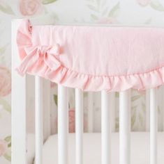 a baby crib with pink ruffled bedding and floral wallpaper in the background