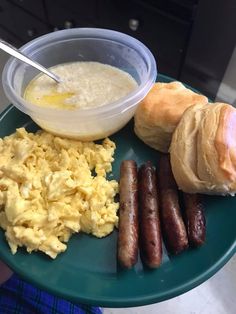 a blue plate topped with eggs, sausages and other breakfast foods next to a roll