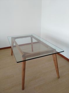 a glass table with wooden legs in an empty room on the floor next to a white wall