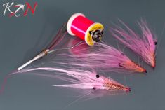 three pink and yellow flies are next to a thread spool on a gray surface