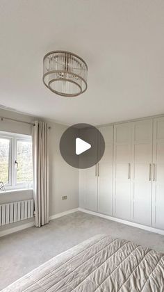 an empty bedroom with white cabinets and a chandelier hanging from the ceiling, in front of a large window