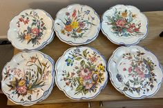 six plates with flowers painted on them are sitting on a wooden table next to a wall