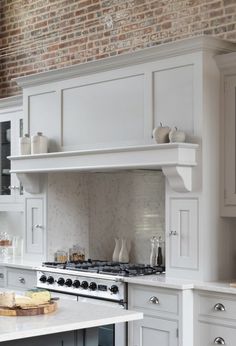 a kitchen with white cabinets and an island in front of a brick wall that has a clock on it