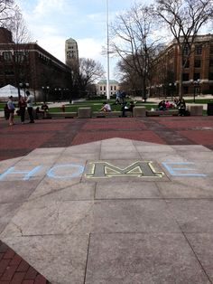 people are sitting on benches in the middle of a park with chalk writing that reads home