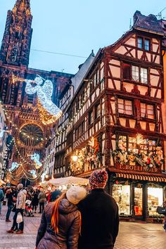 two people are standing in front of an old building with christmas lights on the outside