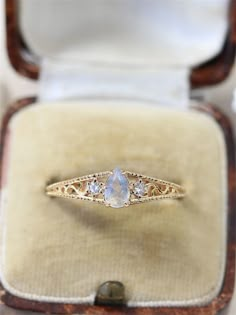 an engagement ring with three pear shaped diamonds on it in a wooden box, sitting on top of a table