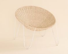 a wicker chair with metal legs and a white frame on the bottom, against a beige background