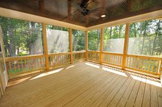 an empty porch with wood flooring and ceiling fan in the center, surrounded by trees