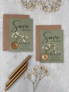 two save the date cards with gold coins and flowers on them next to some pens