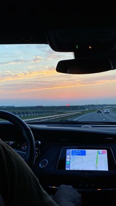 a man driving a car on the highway at sunset with his ipad in front of him