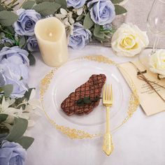 a white table topped with a plate and a fork next to a vase filled with flowers