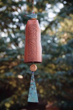 a bird is perched on top of a red bell hanging from a chain in front of some trees