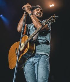 a man holding a guitar while standing on top of a stage with his hands in the air