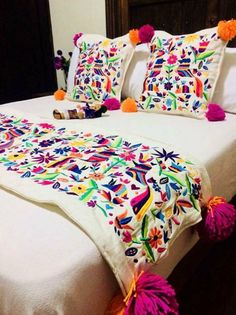 a white bed topped with lots of pillows and colorful decorations on it's headboard